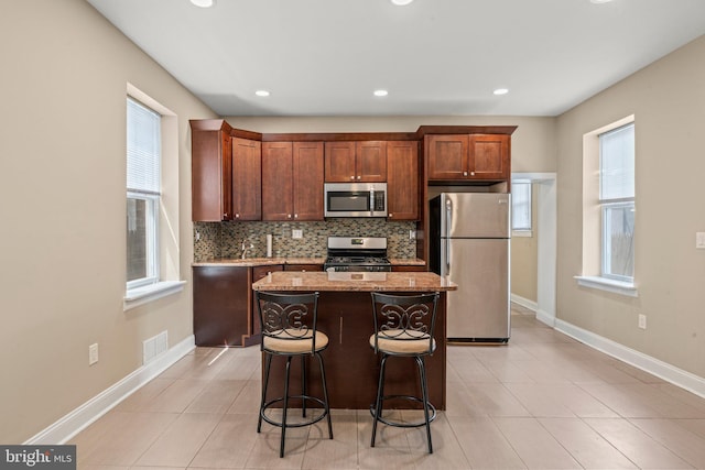 kitchen featuring light stone counters, backsplash, a kitchen bar, a kitchen island, and appliances with stainless steel finishes