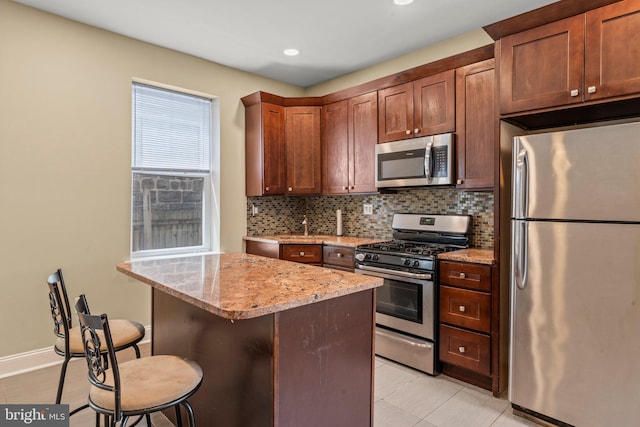 kitchen with a center island, stainless steel appliances, a kitchen breakfast bar, light stone counters, and decorative backsplash