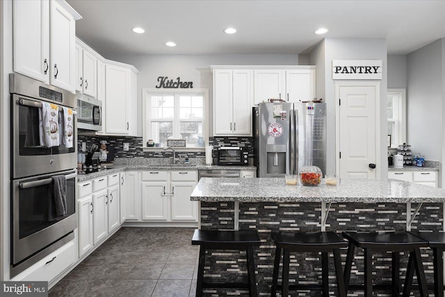 kitchen featuring white cabinets, a kitchen island, light stone counters, and stainless steel appliances