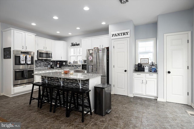 kitchen featuring white cabinetry, a center island, light stone counters, a breakfast bar, and appliances with stainless steel finishes