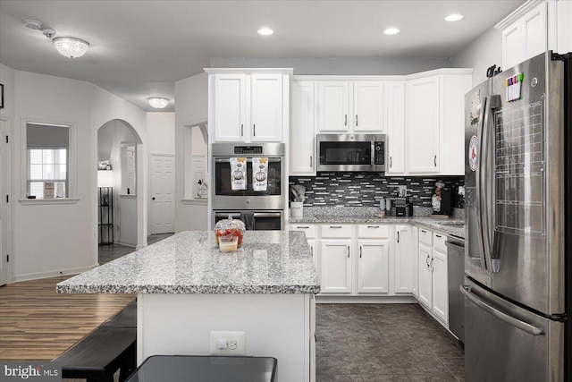 kitchen with a kitchen bar, white cabinetry, light stone counters, and appliances with stainless steel finishes