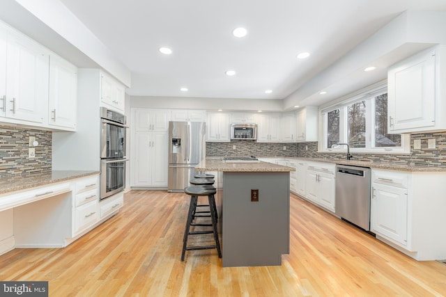 kitchen with appliances with stainless steel finishes, a breakfast bar, white cabinets, a center island, and light stone countertops