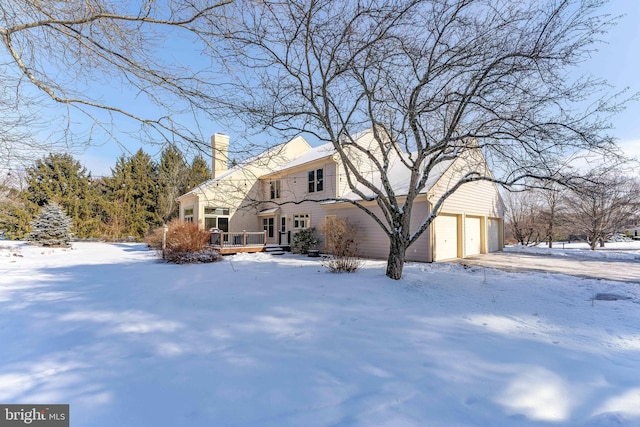 snow covered back of property featuring a wooden deck and a garage