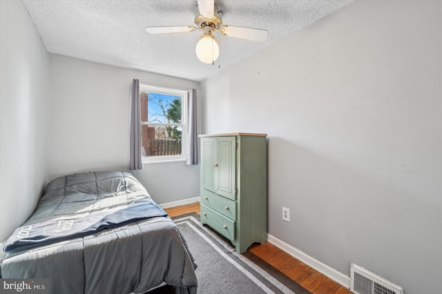 bedroom with a textured ceiling, ceiling fan, and hardwood / wood-style flooring