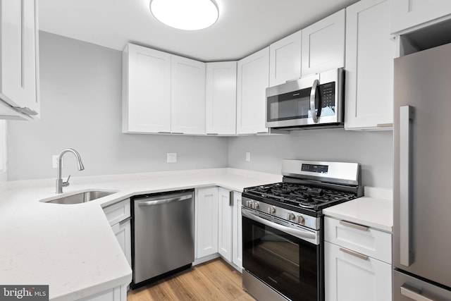 kitchen with sink, kitchen peninsula, light hardwood / wood-style floors, white cabinets, and appliances with stainless steel finishes