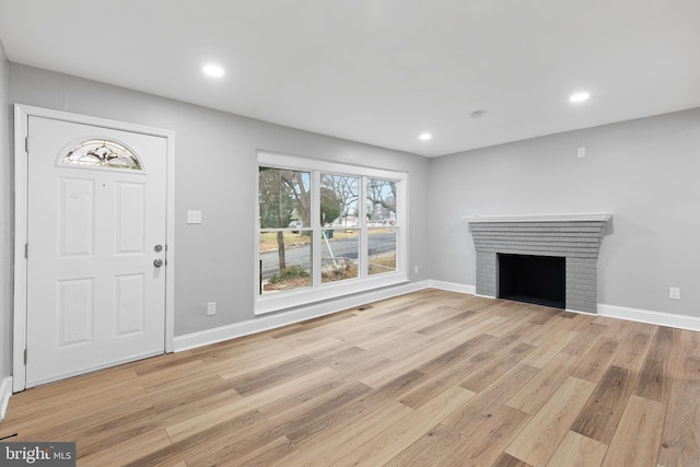 unfurnished living room featuring light wood-type flooring and a brick fireplace