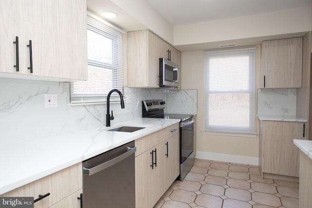 kitchen with light stone countertops, sink, stainless steel appliances, backsplash, and light brown cabinetry