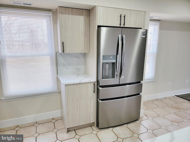 kitchen featuring light stone countertops, light brown cabinetry, and stainless steel refrigerator with ice dispenser