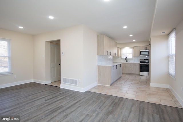 kitchen with tasteful backsplash, stainless steel appliances, sink, light brown cabinets, and light hardwood / wood-style floors