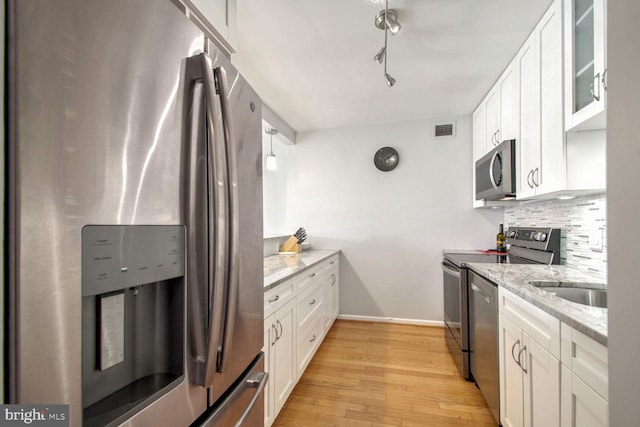 kitchen with light wood-type flooring, backsplash, light stone counters, stainless steel appliances, and white cabinets