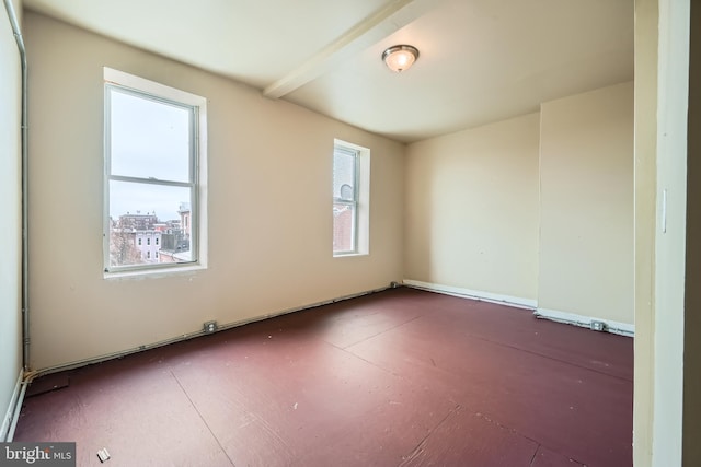 empty room featuring beamed ceiling and a wealth of natural light