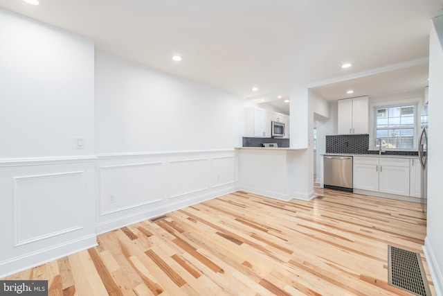 kitchen with backsplash, white cabinets, sink, light hardwood / wood-style flooring, and appliances with stainless steel finishes