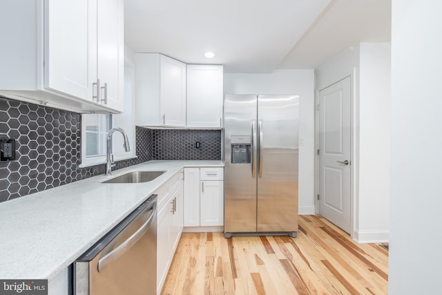 kitchen with appliances with stainless steel finishes, light hardwood / wood-style floors, white cabinetry, and sink