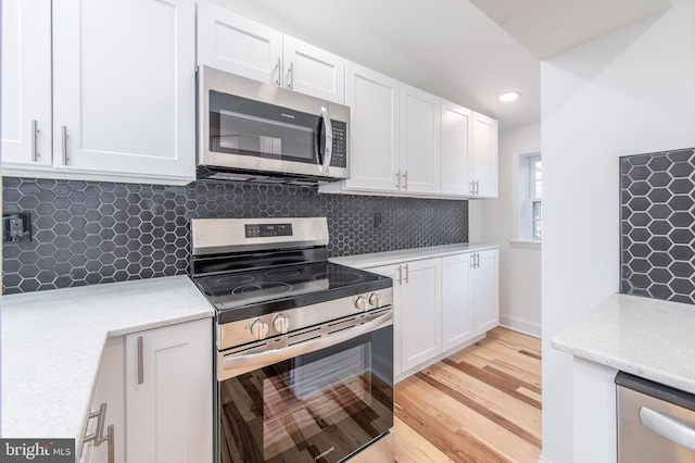 kitchen with light stone countertops, backsplash, stainless steel appliances, light hardwood / wood-style flooring, and white cabinets