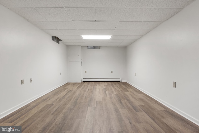 empty room with wood-type flooring, a drop ceiling, and a baseboard heating unit