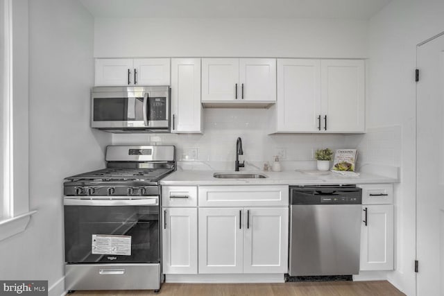 kitchen with appliances with stainless steel finishes, light stone counters, sink, light hardwood / wood-style flooring, and white cabinetry