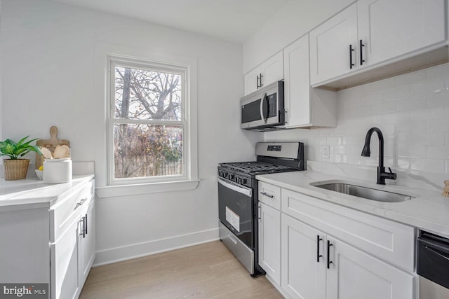 kitchen featuring sink, stainless steel appliances, decorative backsplash, white cabinets, and light wood-type flooring