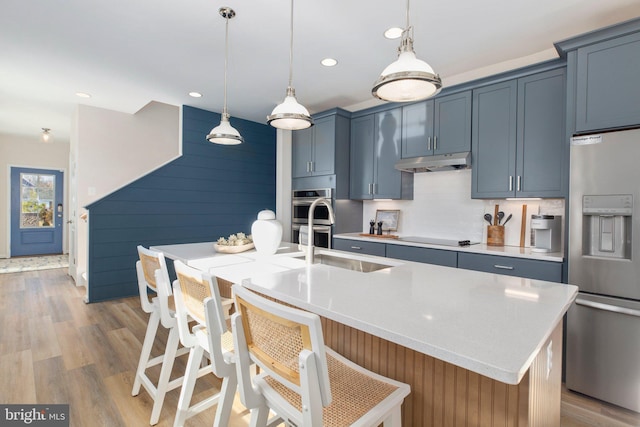 kitchen with blue cabinetry, appliances with stainless steel finishes, light hardwood / wood-style floors, and an island with sink