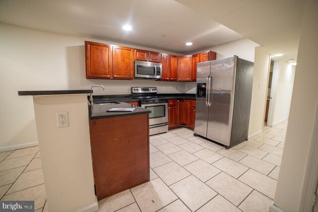 kitchen with light tile patterned flooring, kitchen peninsula, sink, and appliances with stainless steel finishes