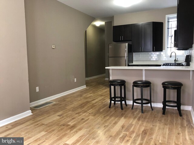 kitchen featuring a breakfast bar, stainless steel fridge, kitchen peninsula, and light hardwood / wood-style floors