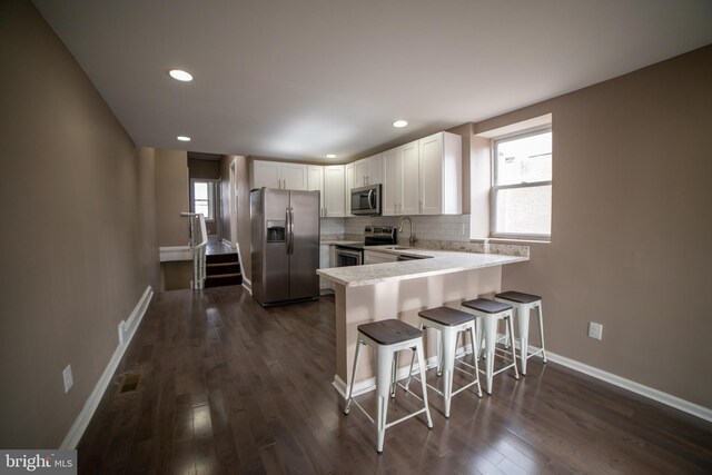 kitchen with a kitchen breakfast bar, stainless steel appliances, white cabinetry, and dark wood-type flooring