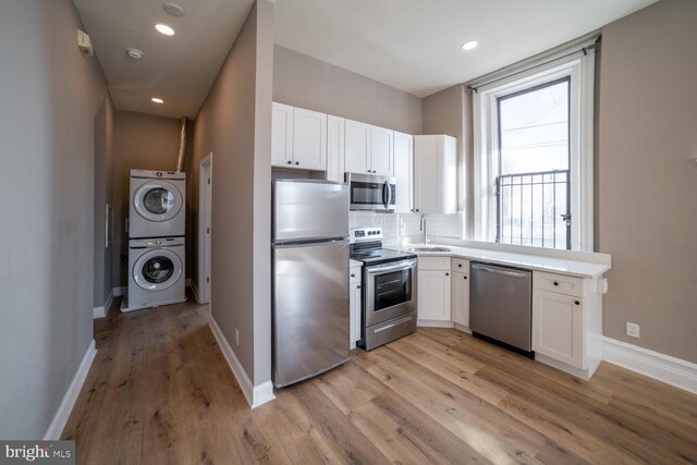 kitchen with stacked washing maching and dryer, white cabinetry, stainless steel appliances, and light hardwood / wood-style flooring