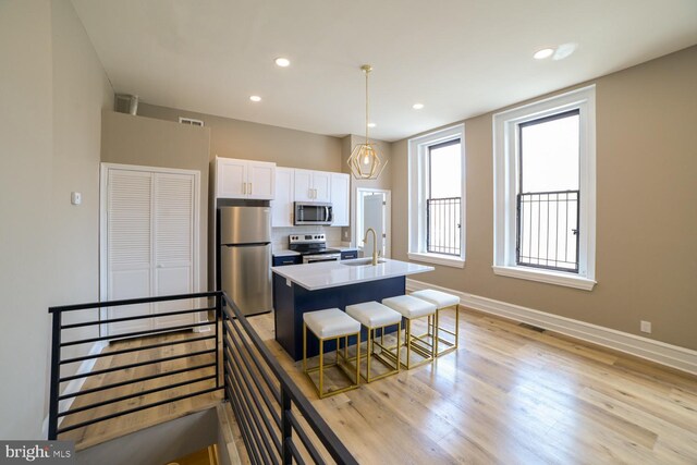 kitchen featuring white cabinetry, sink, stainless steel appliances, pendant lighting, and a kitchen island with sink