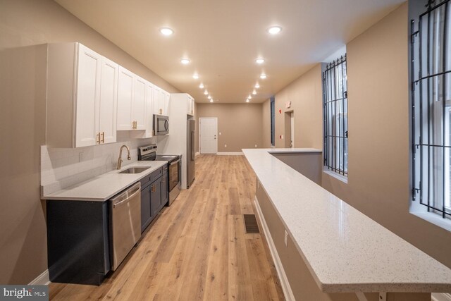 kitchen with tasteful backsplash, stainless steel appliances, sink, light hardwood / wood-style flooring, and white cabinets