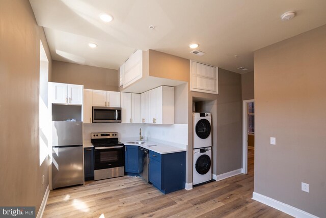 kitchen with appliances with stainless steel finishes, stacked washing maching and dryer, blue cabinets, white cabinets, and light hardwood / wood-style floors