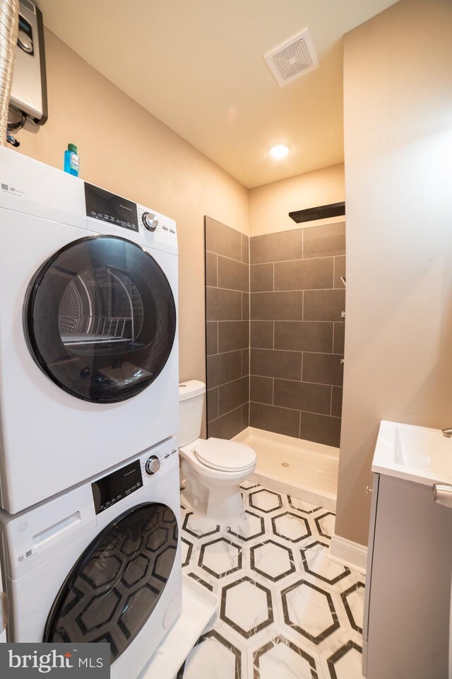 bathroom featuring vanity, stacked washer and clothes dryer, tile patterned floors, toilet, and a tile shower