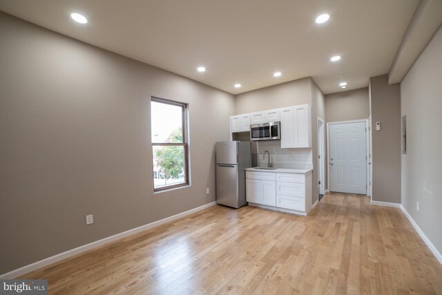 kitchen with white cabinetry, sink, stainless steel appliances, and light hardwood / wood-style flooring