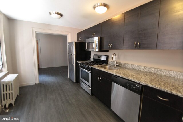 kitchen with dark wood-type flooring, radiator, sink, light stone counters, and stainless steel appliances