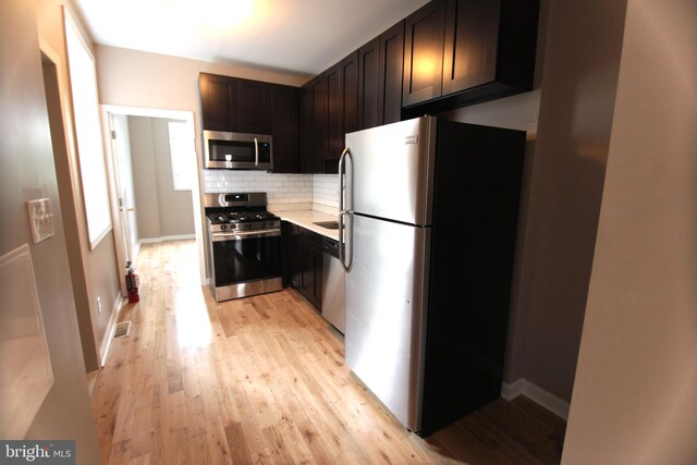 kitchen featuring dark brown cabinetry, light wood-type flooring, backsplash, and appliances with stainless steel finishes