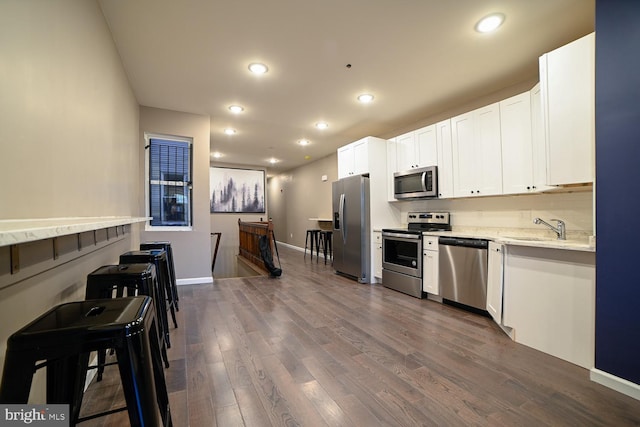 kitchen with white cabinetry, sink, stainless steel appliances, light stone counters, and dark hardwood / wood-style flooring