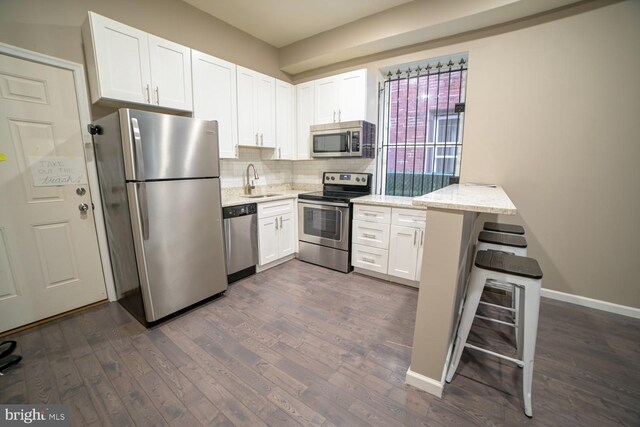 kitchen featuring dark hardwood / wood-style flooring, light stone counters, stainless steel appliances, sink, and white cabinets