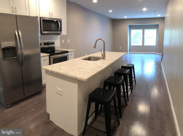 kitchen with a breakfast bar, dark wood-type flooring, a center island with sink, sink, and appliances with stainless steel finishes