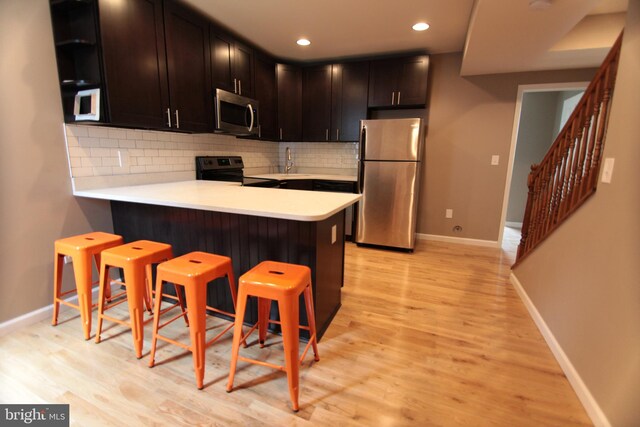 kitchen featuring a breakfast bar, appliances with stainless steel finishes, light wood-type flooring, and kitchen peninsula