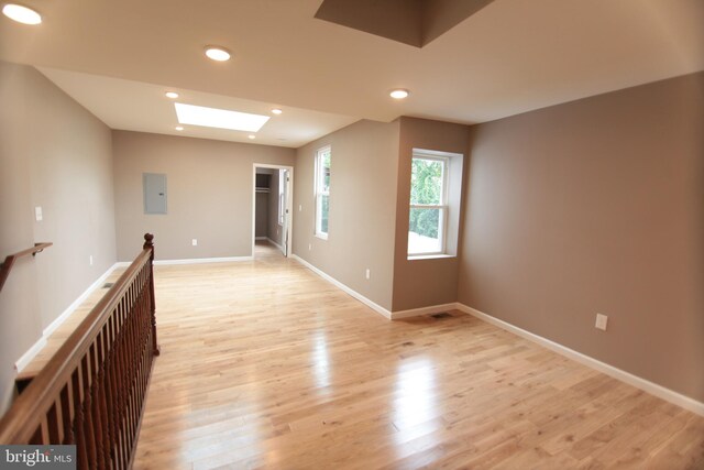 empty room with electric panel, a skylight, and light hardwood / wood-style floors