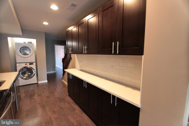 kitchen with dark brown cabinetry, decorative backsplash, stacked washer and dryer, and dark wood-type flooring