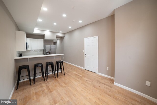 kitchen with light hardwood / wood-style flooring, kitchen peninsula, stainless steel fridge, a kitchen bar, and white cabinets