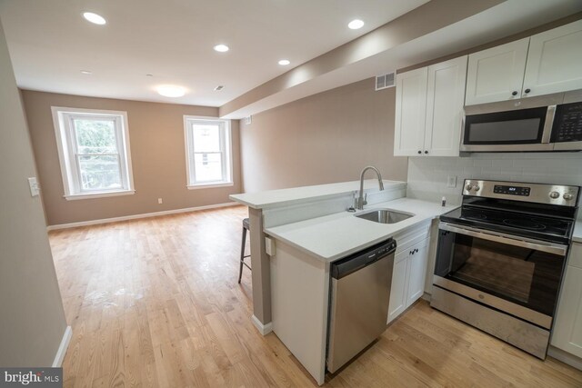 kitchen featuring kitchen peninsula, stainless steel appliances, sink, light hardwood / wood-style flooring, and white cabinets