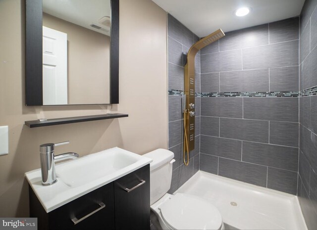 bathroom featuring a tile shower, vanity, and toilet