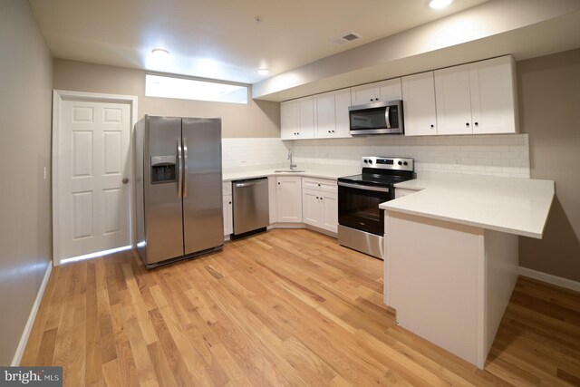 kitchen featuring kitchen peninsula, light wood-type flooring, tasteful backsplash, stainless steel appliances, and white cabinetry