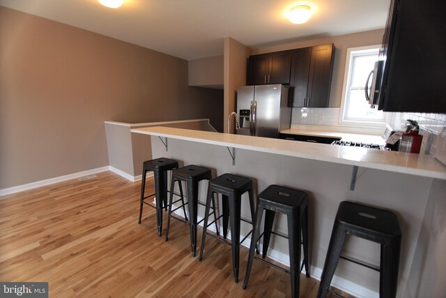 kitchen featuring a kitchen breakfast bar, stainless steel fridge with ice dispenser, kitchen peninsula, and light hardwood / wood-style flooring