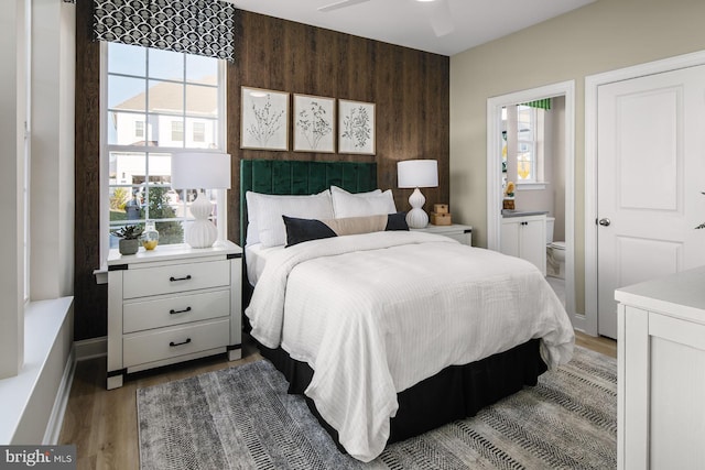 bedroom with ensuite bath, ceiling fan, multiple windows, and hardwood / wood-style flooring