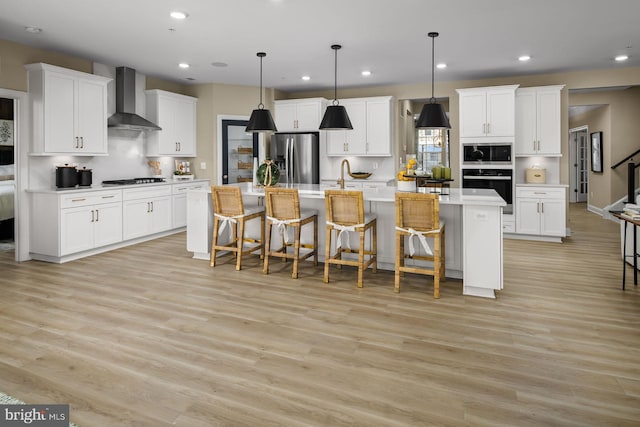 kitchen featuring a center island with sink, wall chimney exhaust hood, white cabinets, and oven