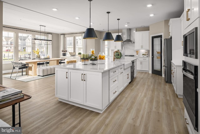 kitchen featuring white cabinetry, wall chimney exhaust hood, hanging light fixtures, stainless steel appliances, and a kitchen island with sink