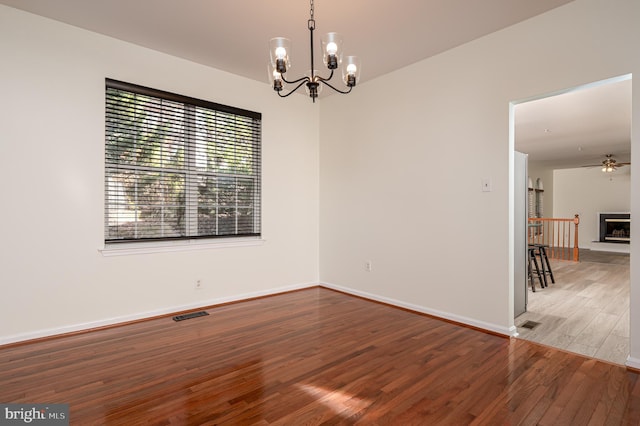 empty room with hardwood / wood-style floors and ceiling fan with notable chandelier