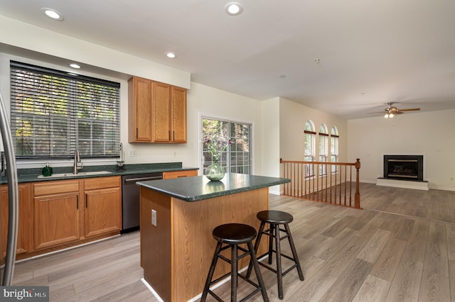 kitchen with a kitchen breakfast bar, sink, stainless steel dishwasher, light wood-type flooring, and a kitchen island