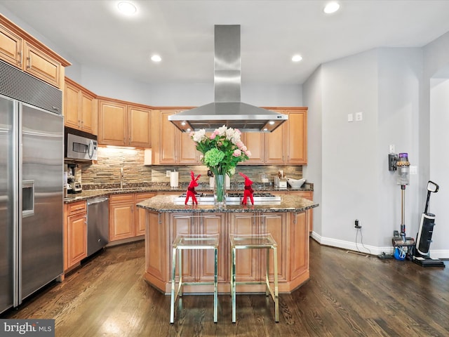 kitchen with island exhaust hood, a kitchen island, dark wood-type flooring, and appliances with stainless steel finishes